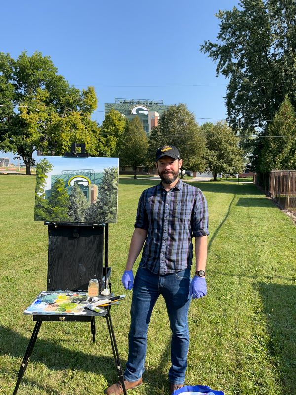 A man painting with an easel in front of Lambeau Field in Green Bay